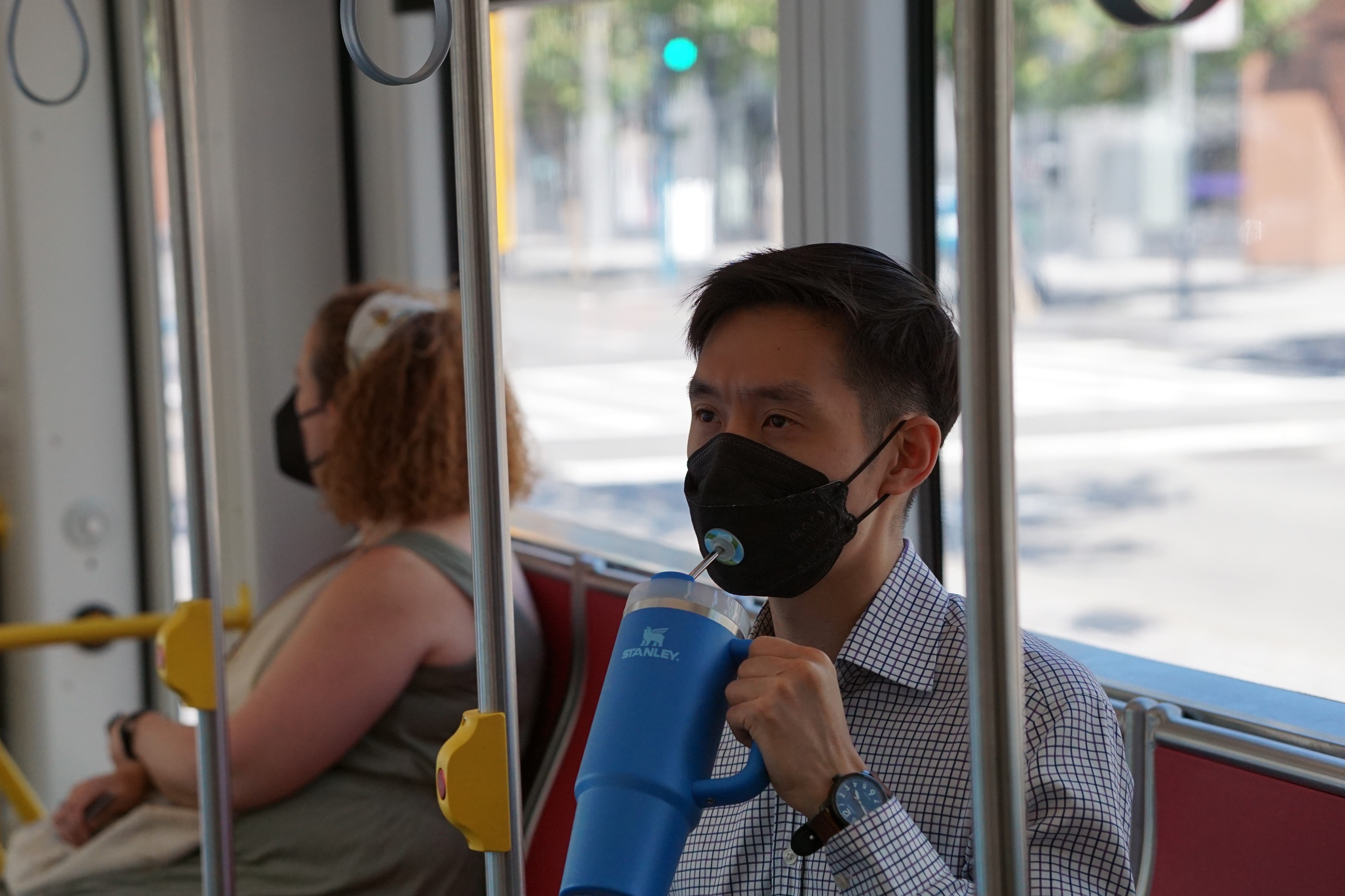 Person drinking on public transit with SIP face mask valve and straw system